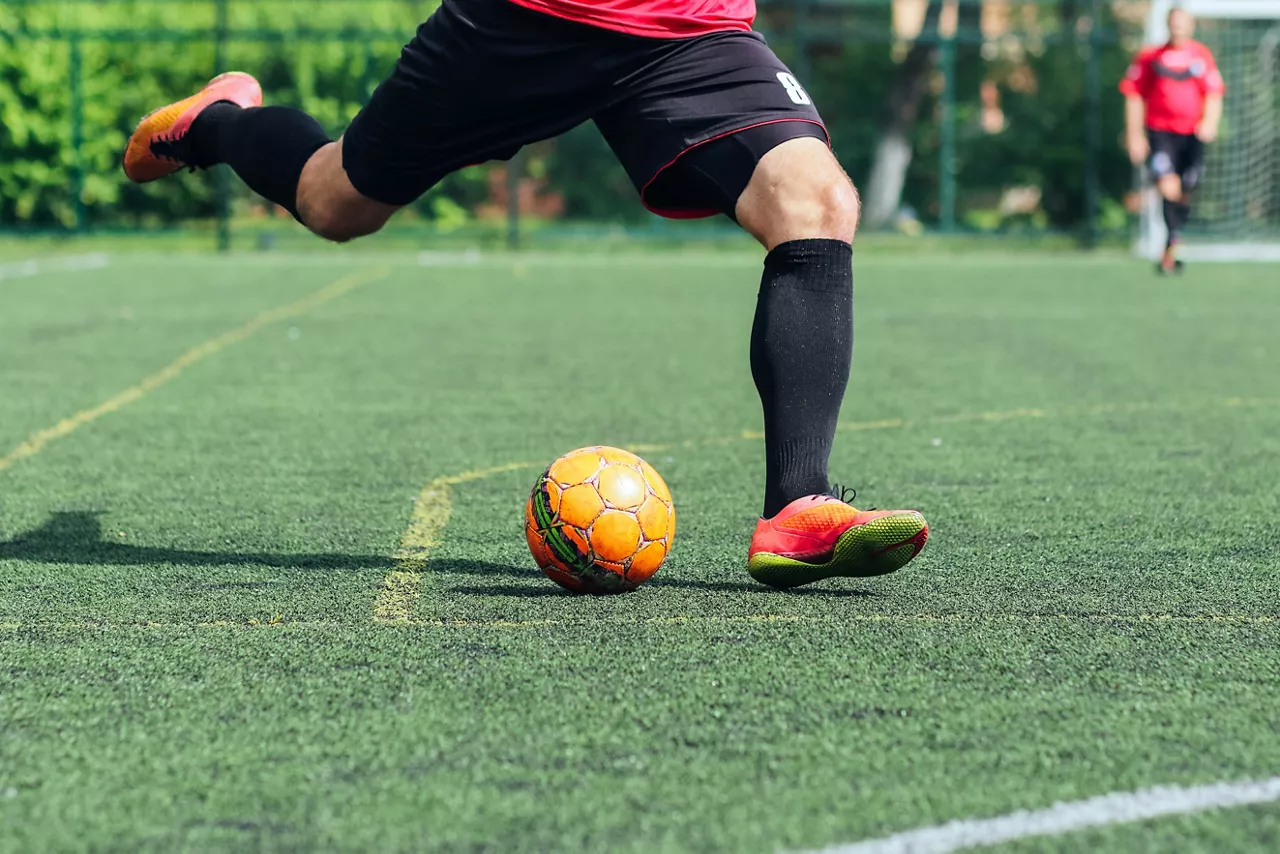 Male soccer player kicking yellow soccer ball on artificial turf