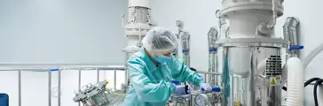Pharmaceutical factory woman worker in protective clothing operating production line in sterile environment
