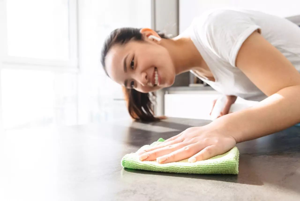 Woman wearing holding sprayer and cleaning table with rag in kitchen at home