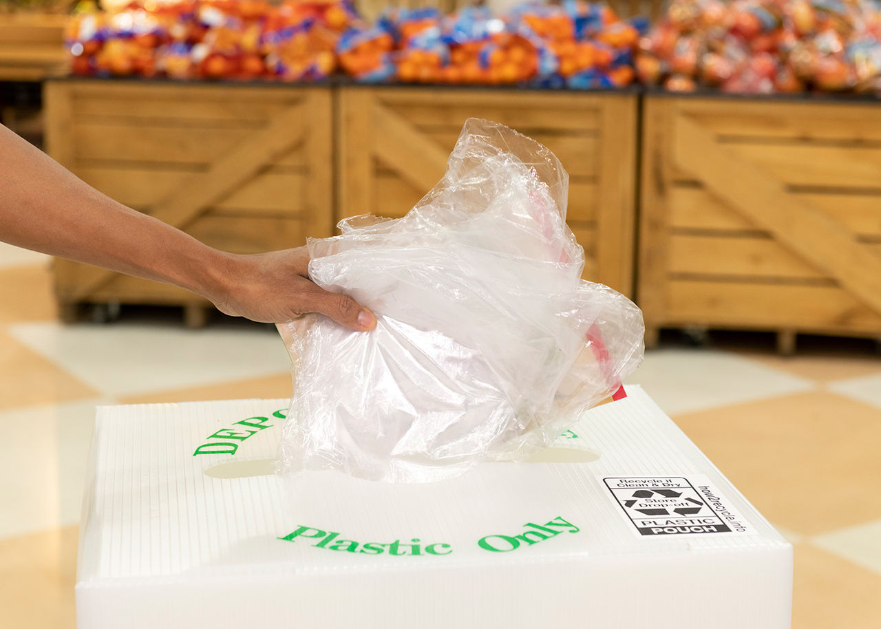 person placing plastic wrap into an in-store recycling container