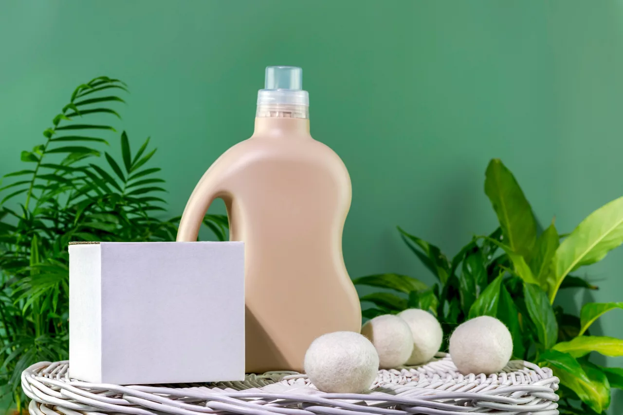 Bottle of detergent or fabric softener and box with detergent powder on a green background with green leaves.